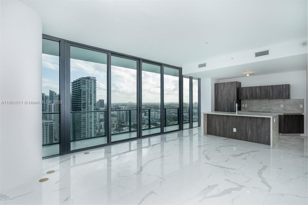 A modern kitchen and living area features white marble floors, dark cabinetry, and floor-to-ceiling windows — 480 NE 31 St # 3101, Miami FL 33137, MIAMI, FL