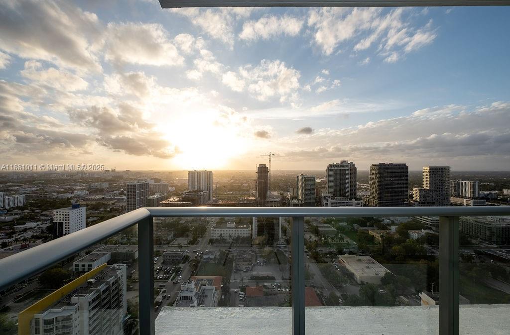 A high-rise balcony overlooks a sprawling city skyline during a bright sunset — 480 NE 31 St # 3101, Miami FL 33137, MIAMI, FL