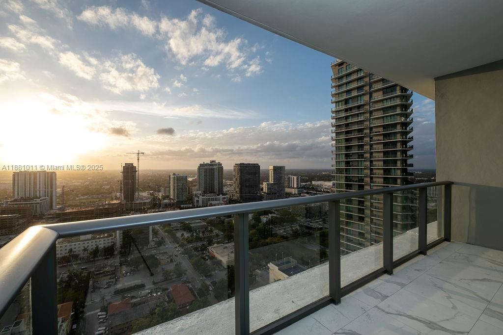 A high-rise balcony with a glass railing overlooks a city skyline at sunset — 480 NE 31 St # 3101, Miami FL 33137, MIAMI, FL