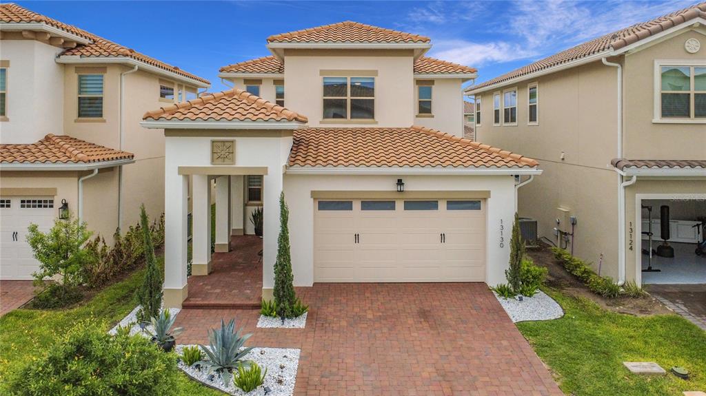 A two-story house with a beige stucco exterior, a tiled roof, and a paved driveway — 13130 WEAVER AVENUE, ORLANDO, FL