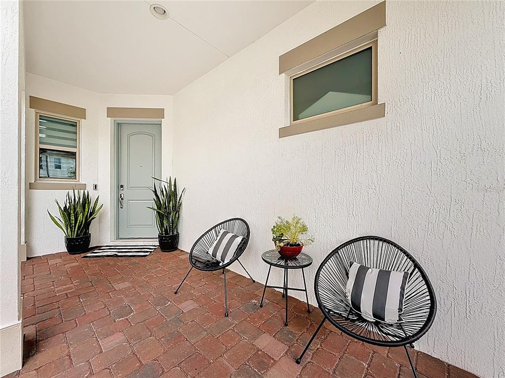 A covered brick porch features two black chairs, a small table, and a light blue door — 13130 WEAVER AVENUE, ORLANDO, FL