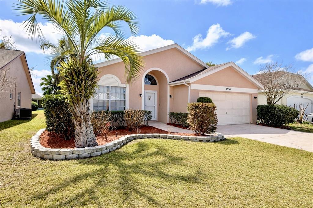 A single-story house with a peach stucco exterior, a palm tree, and a stone-bordered garden — 7830 BECKET ST, NEW PORT RICHEY, FL
