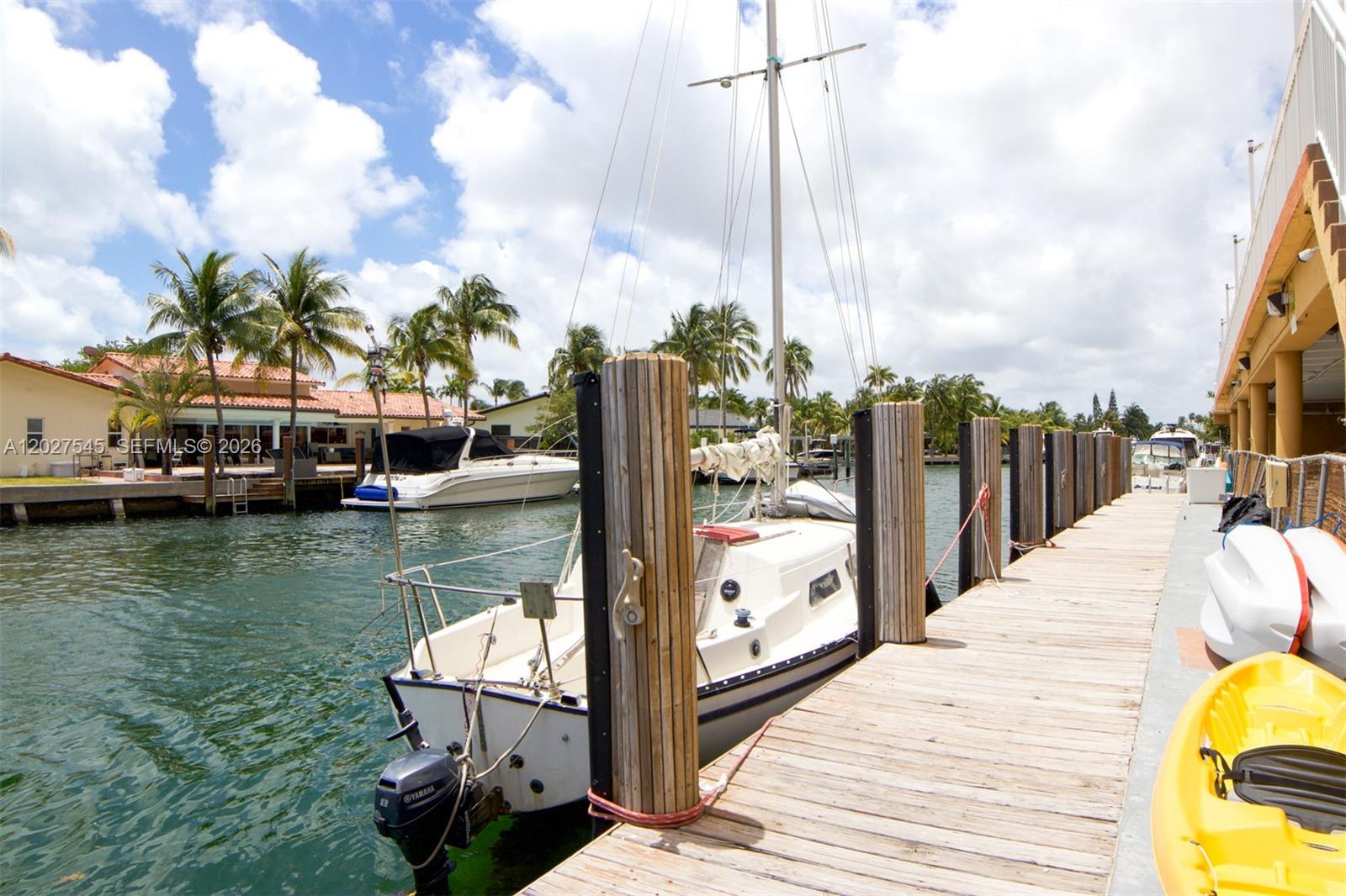 A sailboat is docked at a wooden pier alongside a canal with palm trees — NORTH MIAMI, FL