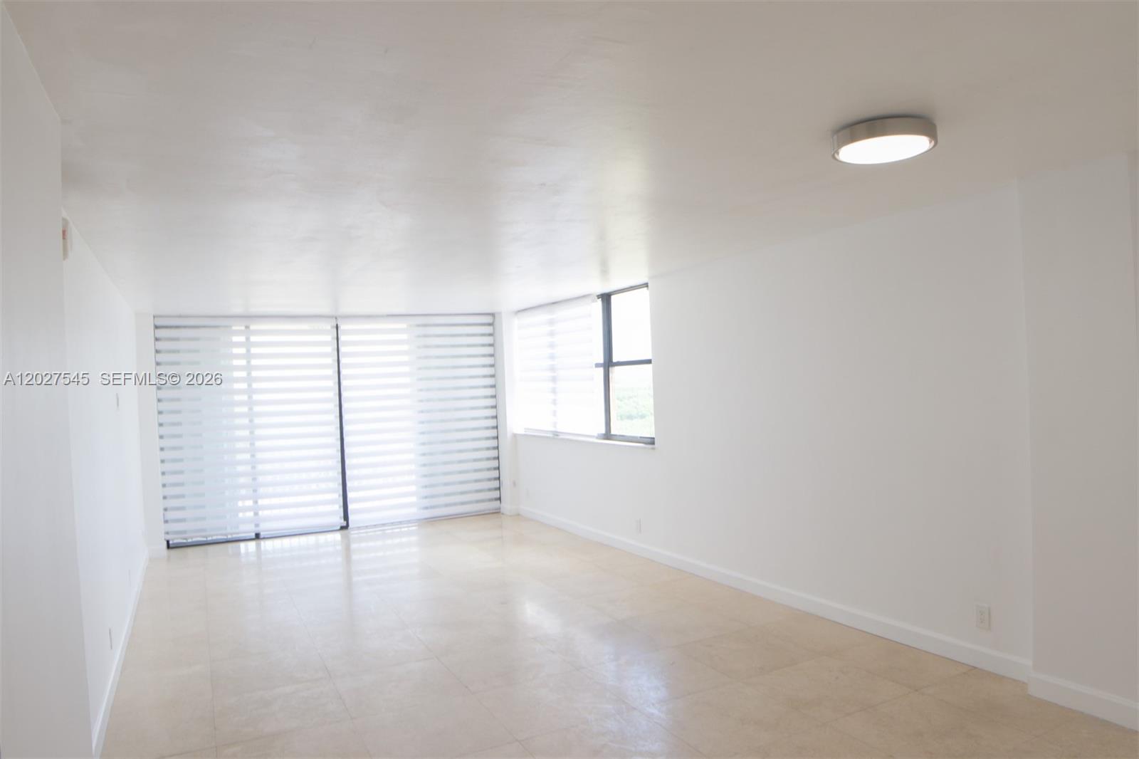 An empty room with white walls, tile flooring, a ceiling light, and large windows — NORTH MIAMI, FL