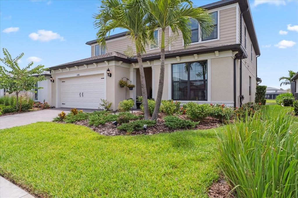 A two-story house with a beige exterior, a two-car garage, and palm trees in front — 2596 BUCKTHORN LOOP, NORTH PORT, FL