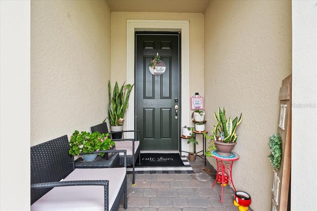 A covered entryway features a dark green front door, patio furniture, and potted plants — 2596 BUCKTHORN LOOP, NORTH PORT, FL
