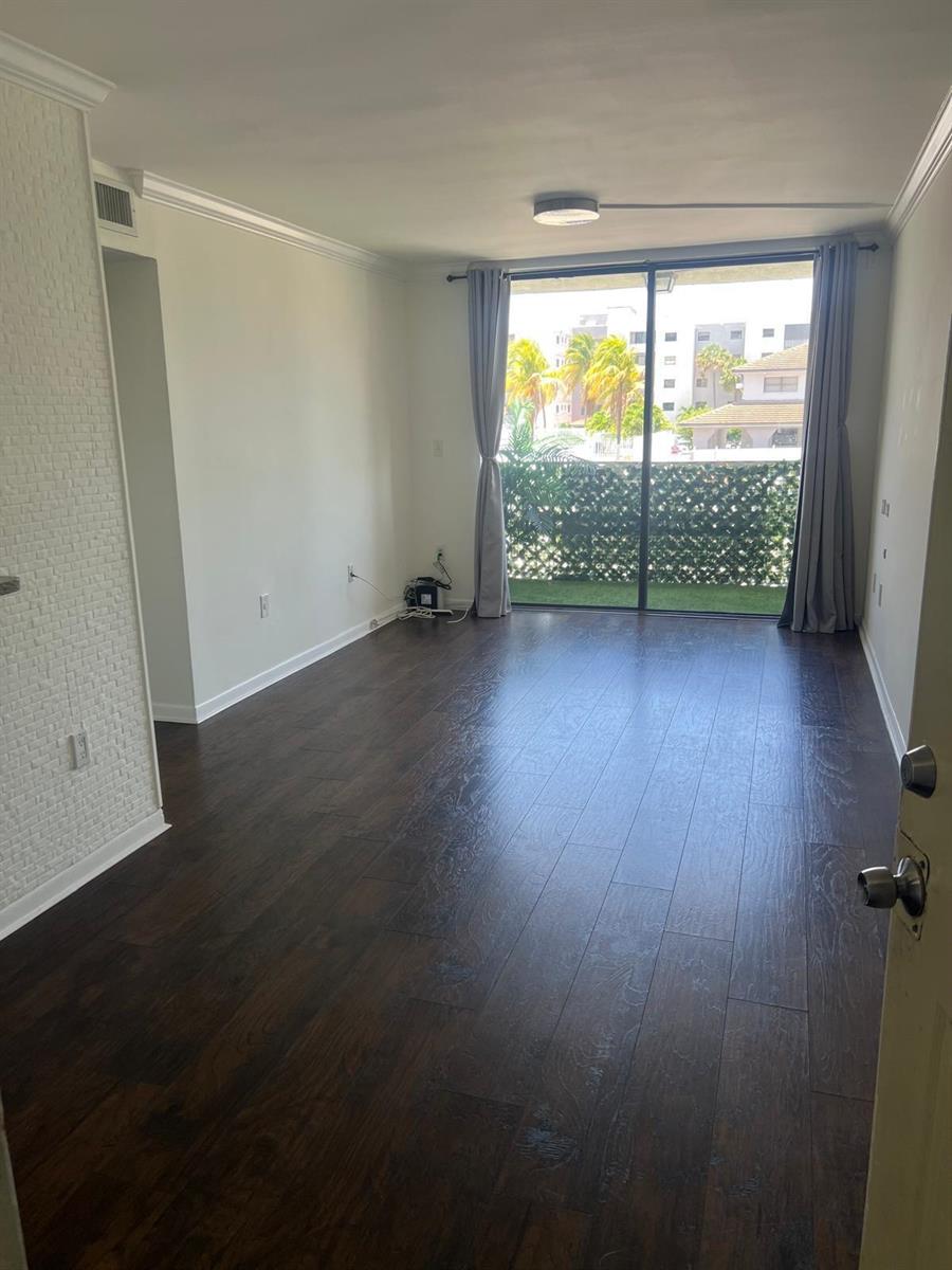 An empty living room features dark wood flooring, white walls, and a sliding glass balcony door — 8145 NW 7th Street # 208, Miami FL 33126, MIAMI, FL