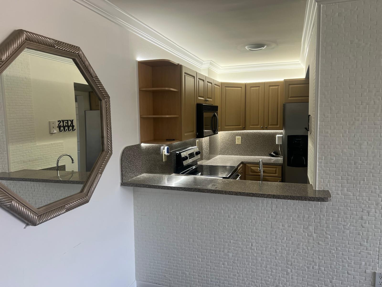 A kitchen with wood cabinets, granite countertops, and white brick-patterned walls viewed past a mirror — 8145 NW 7th Street # 208, Miami FL 33126, MIAMI, FL