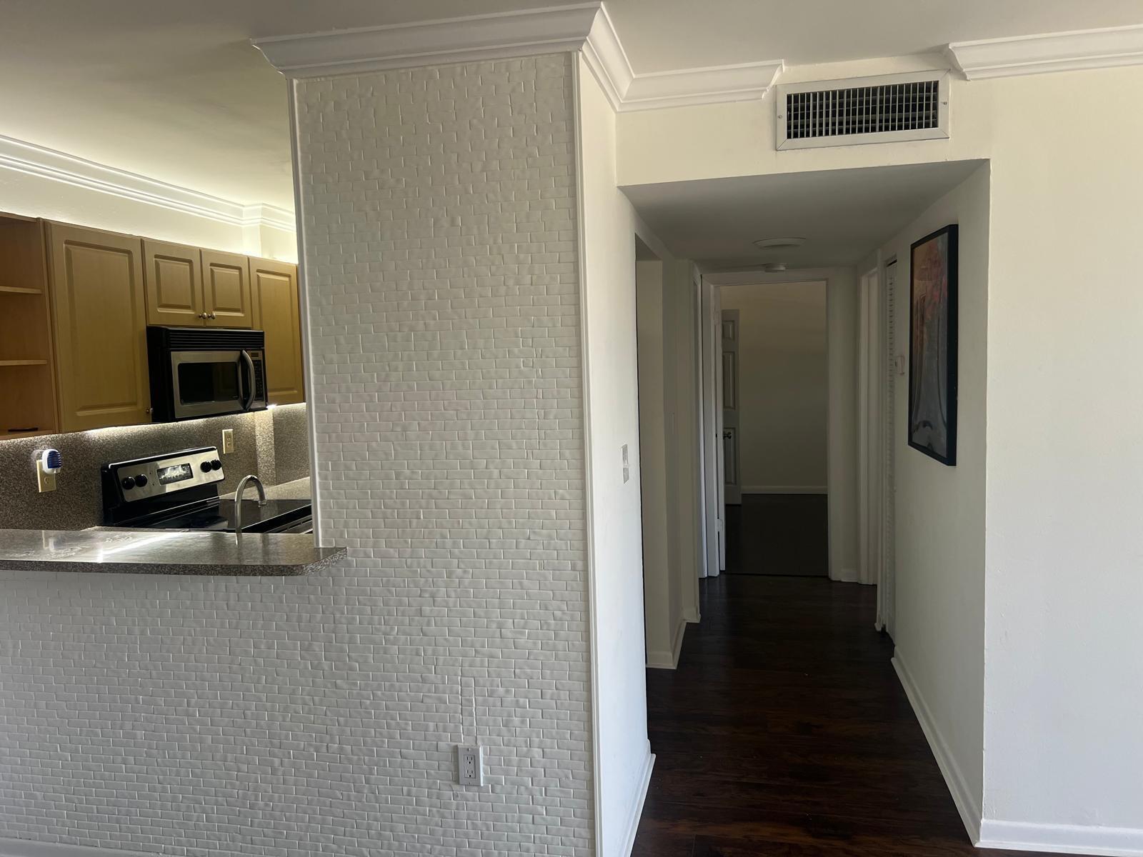 A kitchen with light wood cabinets and a textured white wall overlooks a dark hallway — 8145 NW 7th Street # 208, Miami FL 33126, MIAMI, FL