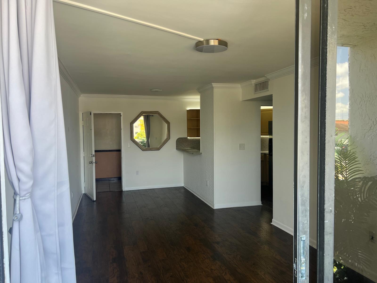 An interior view of a living area with dark wood floors, an octagonal mirror, and kitchen — 8145 NW 7th Street # 208, Miami FL 33126, MIAMI, FL