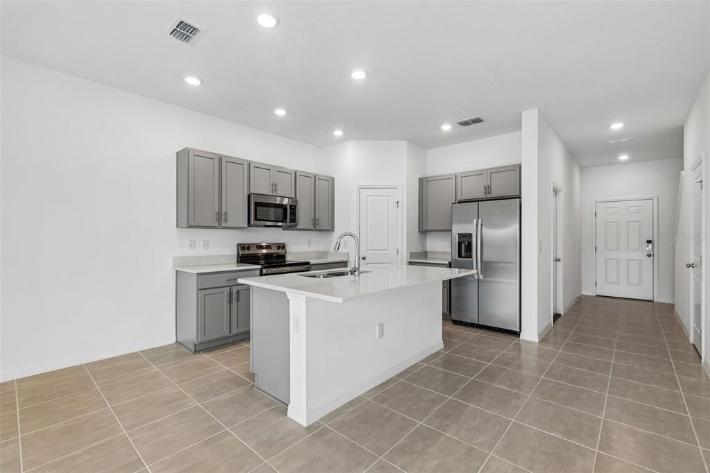 A modern kitchen features gray cabinets, stainless steel appliances, a white island, and tile flooring — 13159 STABLE PLACE, PARRISH, FL