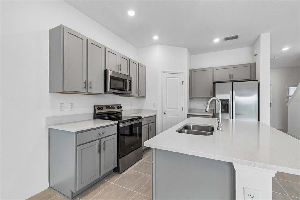 A kitchen features gray cabinets, stainless steel appliances, a center island, and white countertops — 13159 STABLE PLACE, PARRISH, FL