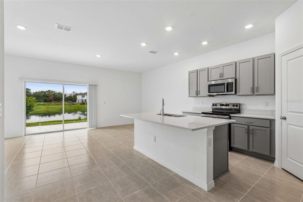 A kitchen with gray cabinets, white countertops, and an island overlooking a pond through sliding doors — 13159 STABLE PLACE, PARRISH, FL