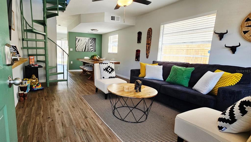 A living room features a spiral staircase, wood-look flooring, and a dark sofa — 10213 N OJUS DRIVE, TAMPA, FL