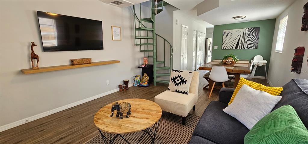 A living and dining area features a spiral staircase, wood flooring, and a wall-mounted television — 10213 N OJUS DRIVE, TAMPA, FL