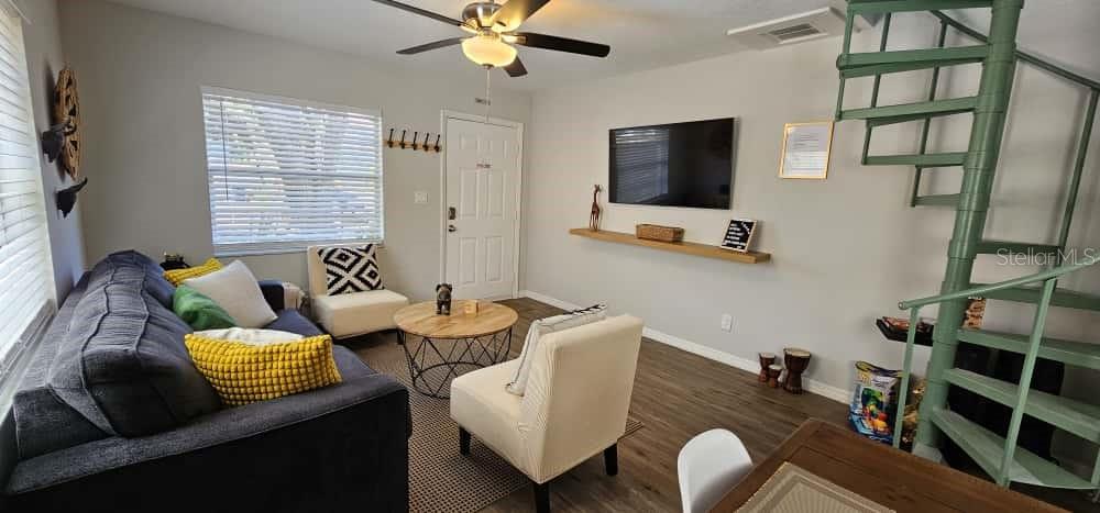 A living room features a dark sofa, two armchairs, a spiral staircase, and a wall-mounted television — 10213 N OJUS DRIVE, TAMPA, FL