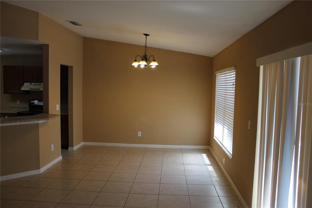 An empty dining area features tan walls, tile flooring, a chandelier, and vertical blinds — 11111 BRAMBLEBRUSH STREET, TAMPA, FL