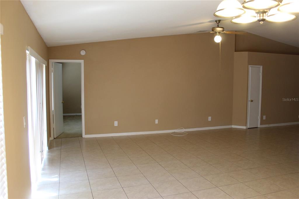 An empty room with tan walls, tile flooring, a ceiling fan, and a sliding glass door — 11111 BRAMBLEBRUSH STREET, TAMPA, FL