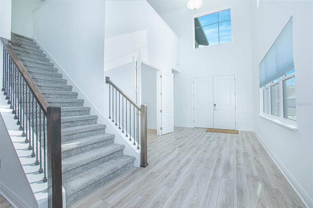 A bright foyer features light wood-look flooring, a carpeted staircase, and a high ceiling — 12034 SPRITE LANE, ORLANDO, FL