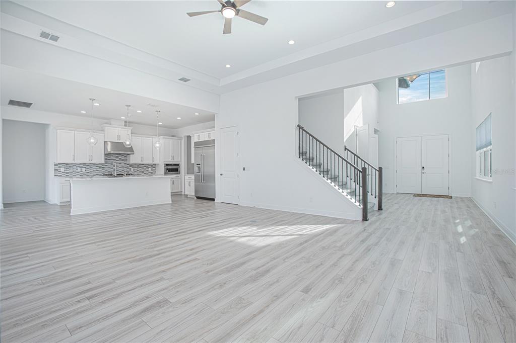 An open-concept living area features light wood-look flooring, a modern kitchen, and a staircase — 12034 SPRITE LANE, ORLANDO, FL
