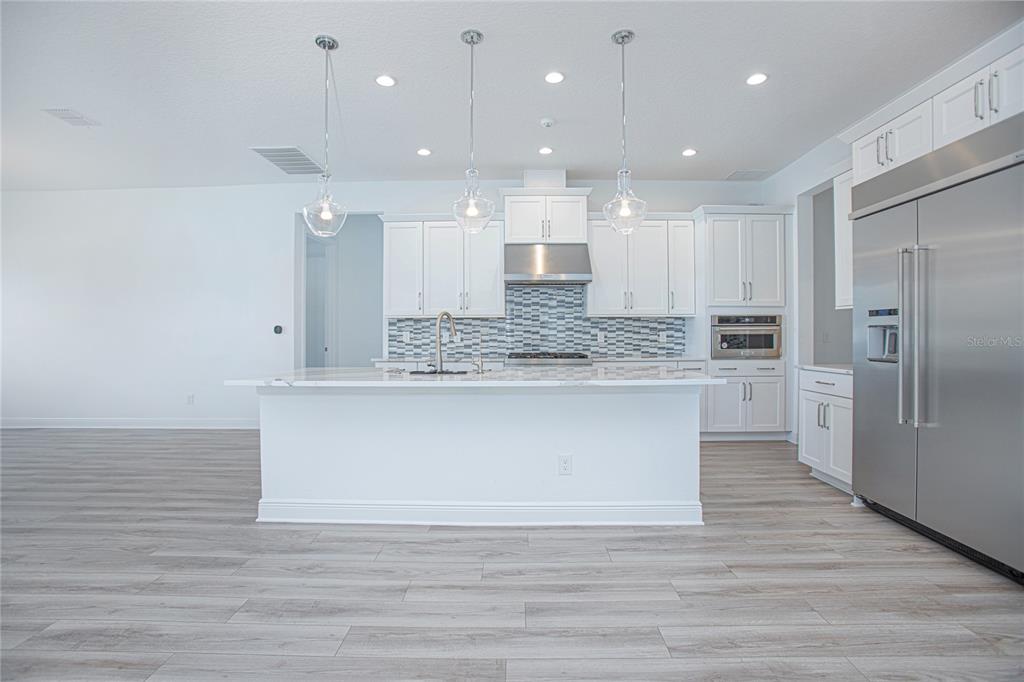A modern kitchen features white cabinetry, a marble-topped island, stainless steel appliances, and wood flooring — 12034 SPRITE LANE, ORLANDO, FL