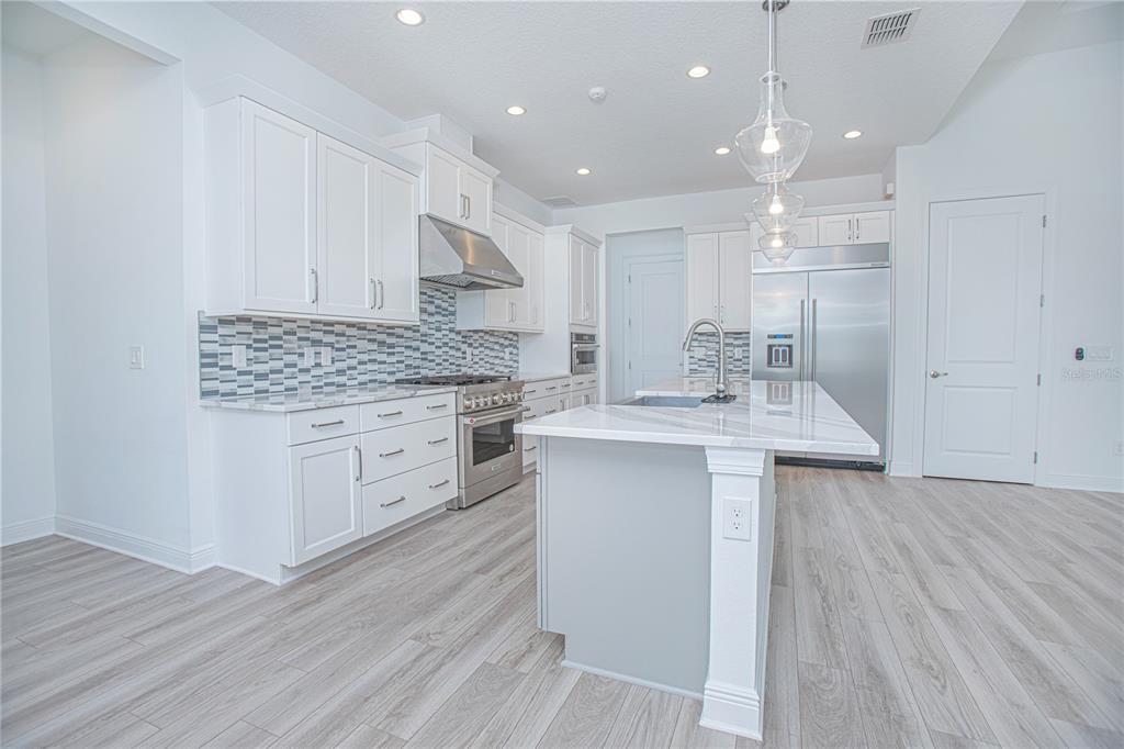 A modern kitchen features white cabinetry, stainless steel appliances, a marble island, and gray flooring — 12034 SPRITE LANE, ORLANDO, FL