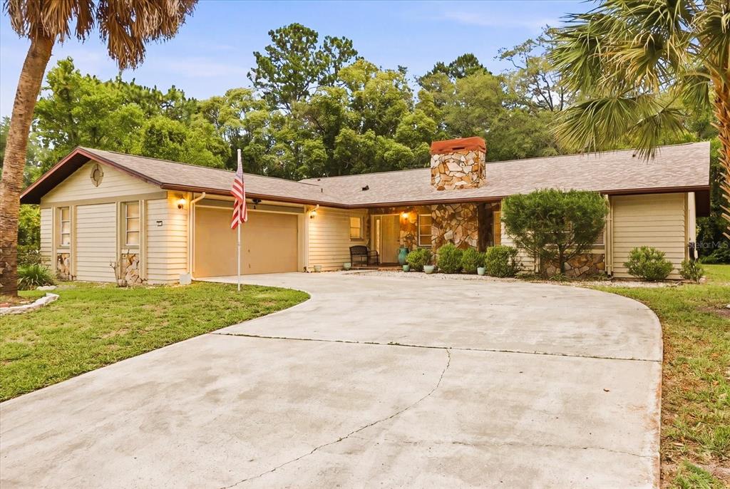 A single-story house with a stone chimney, beige siding, and a concrete driveway — 5 SYCAMORE COURT N, HOMOSASSA, FL