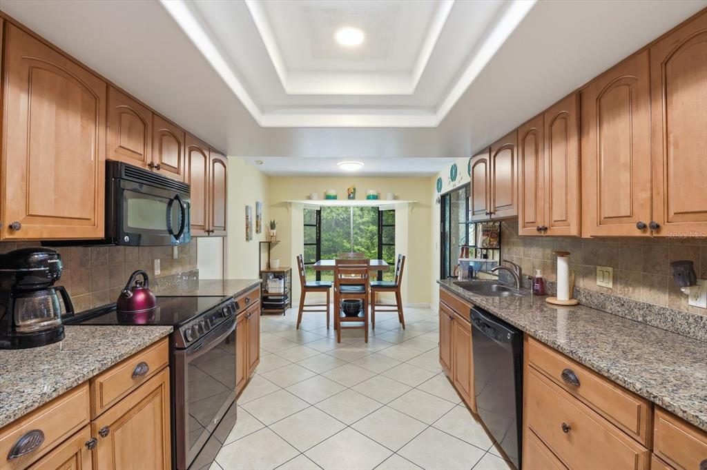A galley kitchen with wood cabinets, granite countertops, and a dining area with a window — 5 SYCAMORE COURT N, HOMOSASSA, FL