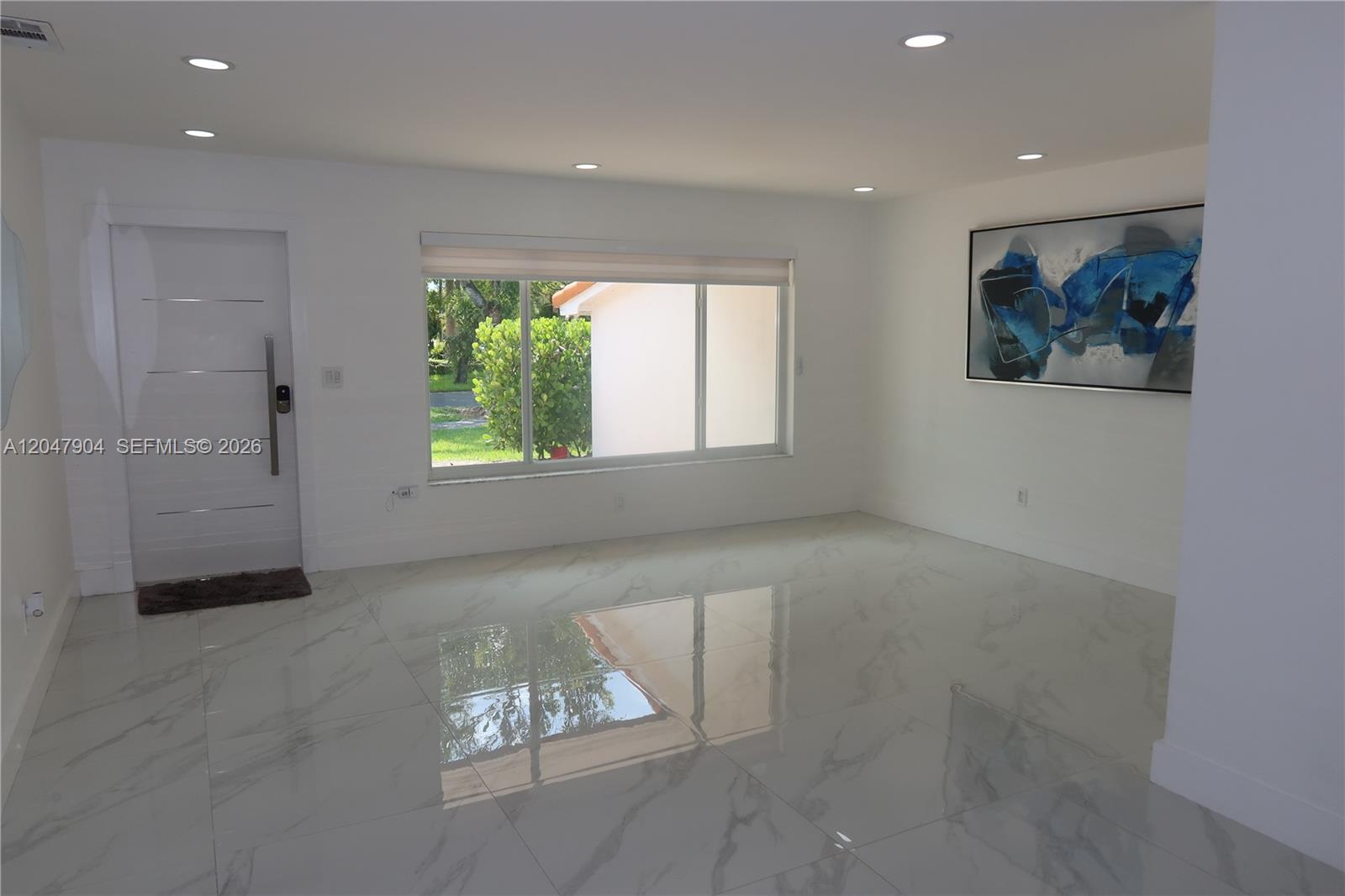 A bright, minimalist room features white walls, large marble-look floor tiles, and a modern front door — 4401 SW 102nd Pl, Miami FL 33165, MIAMI, FL