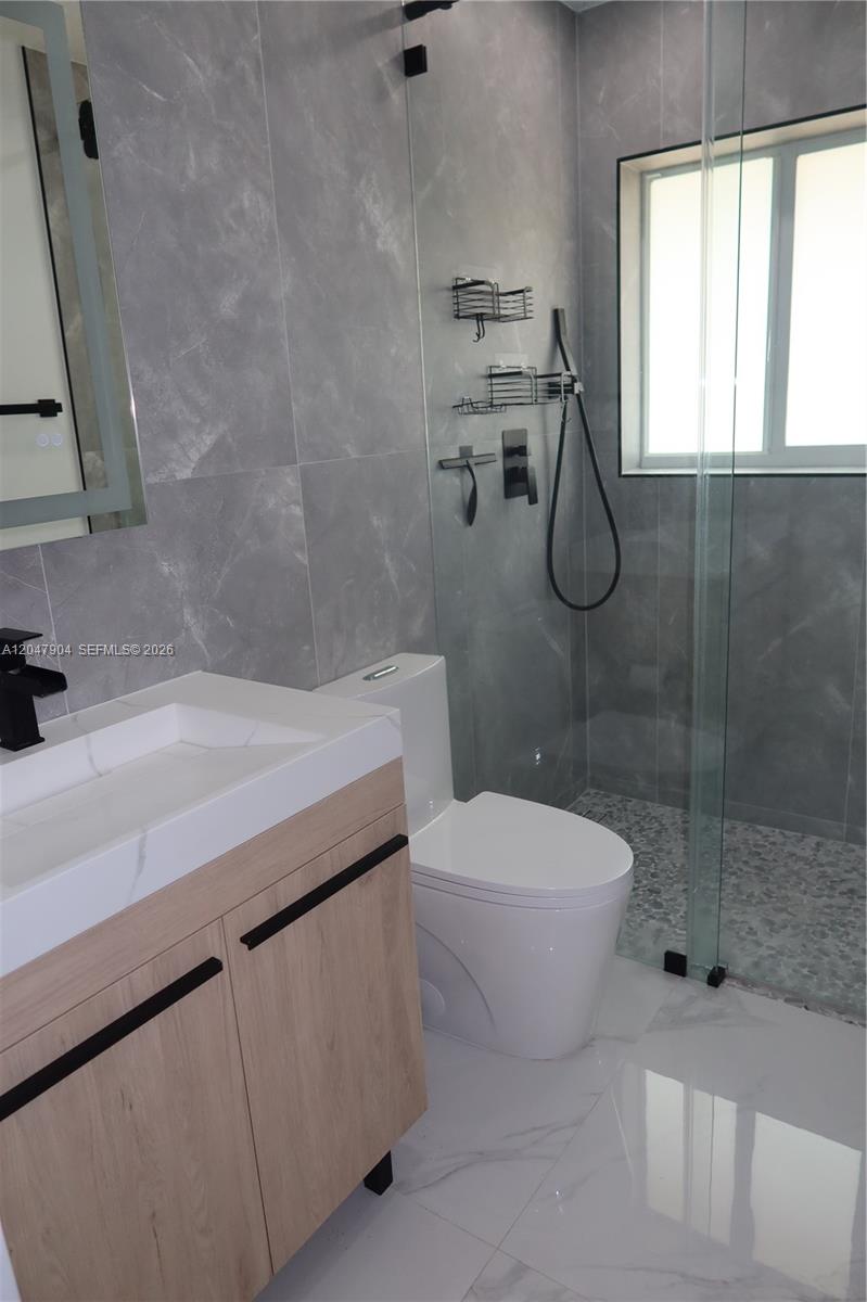 A modern bathroom features a wood vanity, a white toilet, and a glass-enclosed shower — 4401 SW 102nd Pl, Miami FL 33165, MIAMI, FL