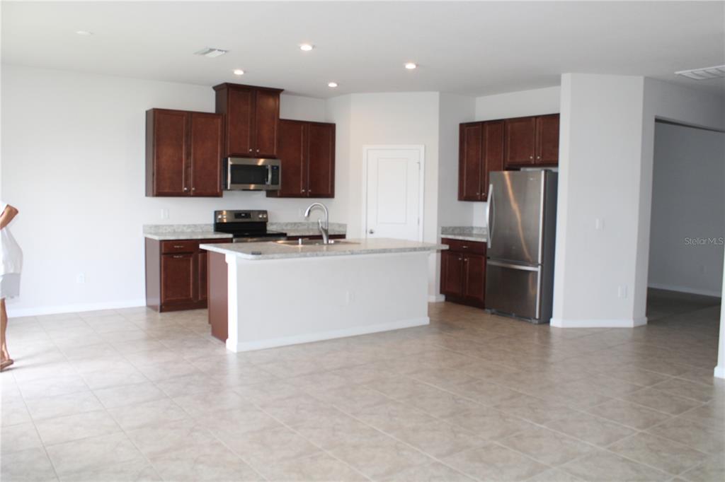 A kitchen features dark wood cabinets, stainless steel appliances, a center island, and tile flooring — 18337 FALLING PINE NEEDLE LANE, LAND O LAKES, FL