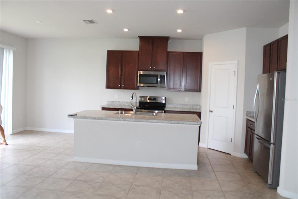 A kitchen features dark wood cabinets, stainless steel appliances, a center island, and tile flooring — 18337 FALLING PINE NEEDLE LANE, LAND O LAKES, FL