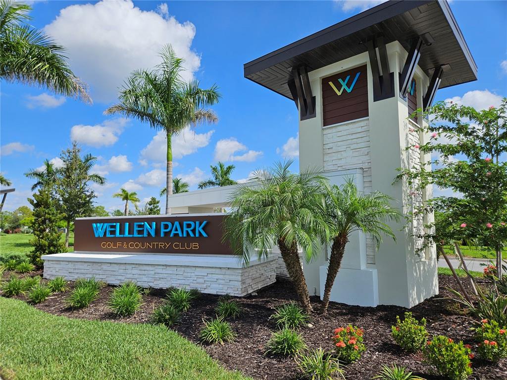 A stone monument sign for Wellen Park Golf & Country Club stands near palm trees — 17685 BORACAY COURT UNIT 101, VENICE, FL