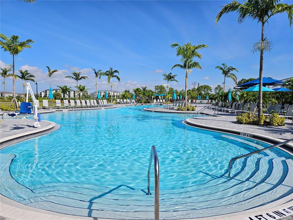 A large outdoor swimming pool with lounge chairs, palm trees, and blue umbrellas — 17685 BORACAY COURT UNIT 101, VENICE, FL