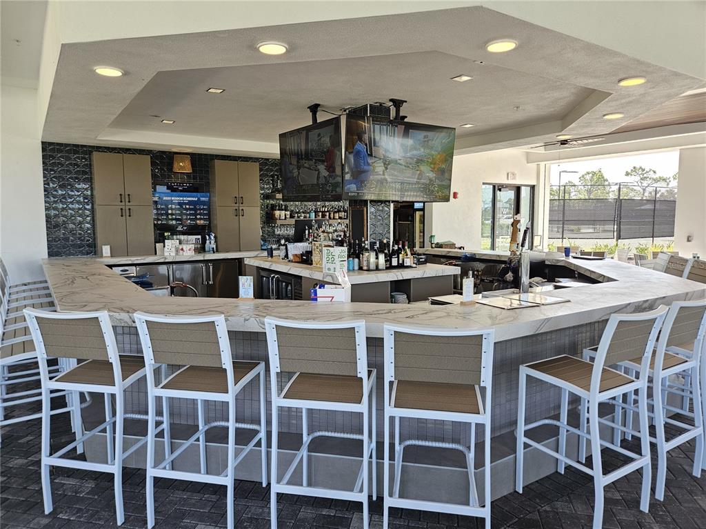 An outdoor bar area features a marble countertop, white chairs, and mounted televisions — 17685 BORACAY COURT UNIT 101, VENICE, FL