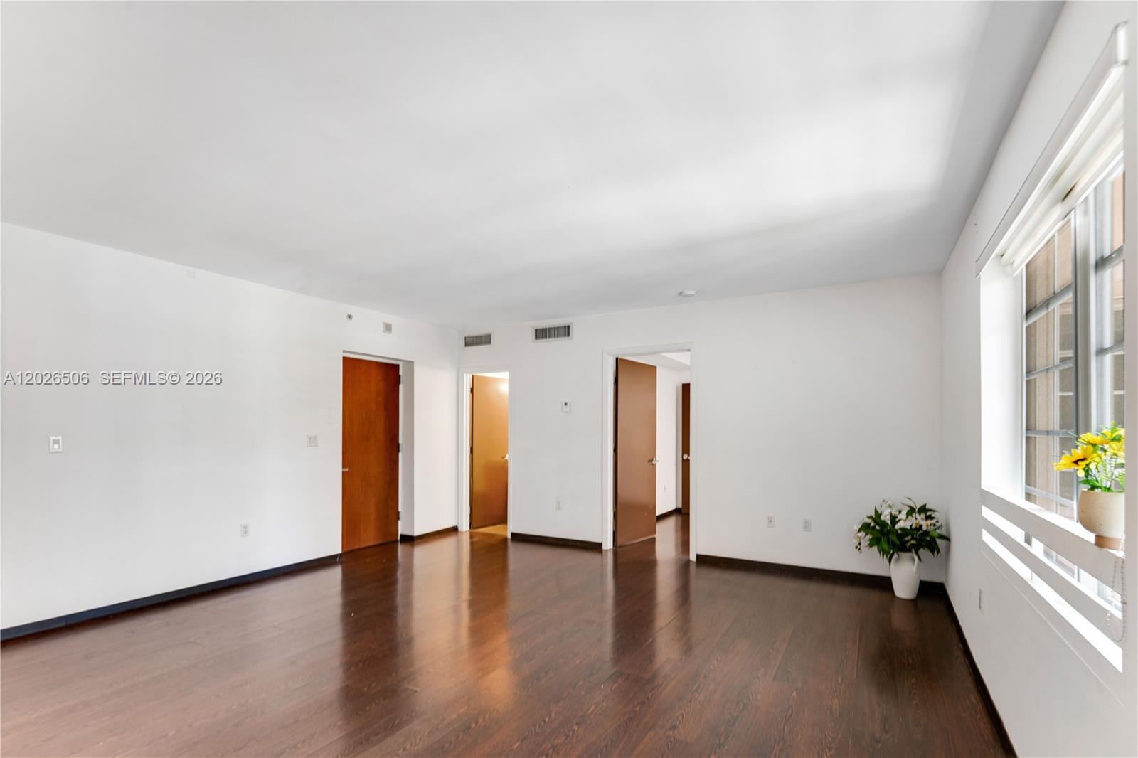 An empty room features white walls, dark hardwood floors, and a window with a plant — 435 21st St # 212, Miami Beach FL 33139, MIAMI BEACH, FL