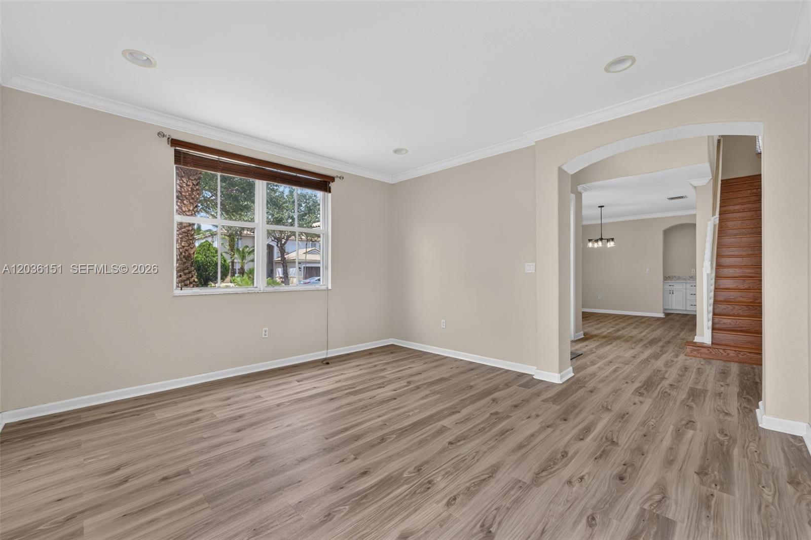 An empty room features light-colored walls, wood-look flooring, a window, and an arched entryway — 1611 SE 16th St, Homestead FL 33035, HOMESTEAD, FL