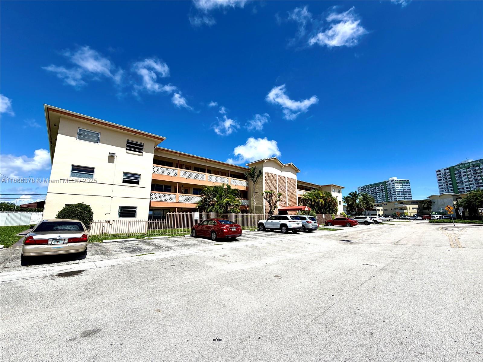 A multi-story apartment building with a parking lot in front under a blue sky — 1885 NE 121st St # 3, North Miami FL 33181, NORTH MIAMI, FL