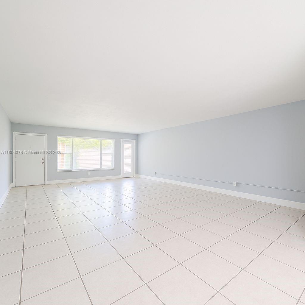 An empty living room features light blue walls, white tile flooring, and a large window — 1885 NE 121st St # 3, North Miami FL 33181, NORTH MIAMI, FL