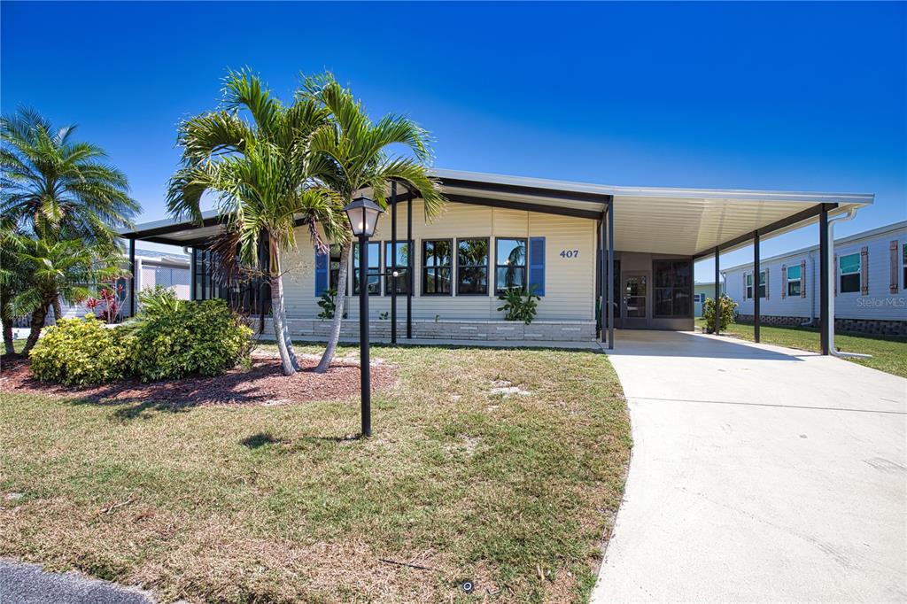 A single-story manufactured home features a carport, a screened porch, and a palm tree — 407 MADONNA, NORTH PORT, FL