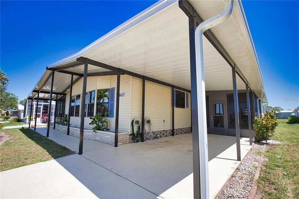 A manufactured home features a large covered carport, light siding, and a screened-in porch area — 407 MADONNA, NORTH PORT, FL