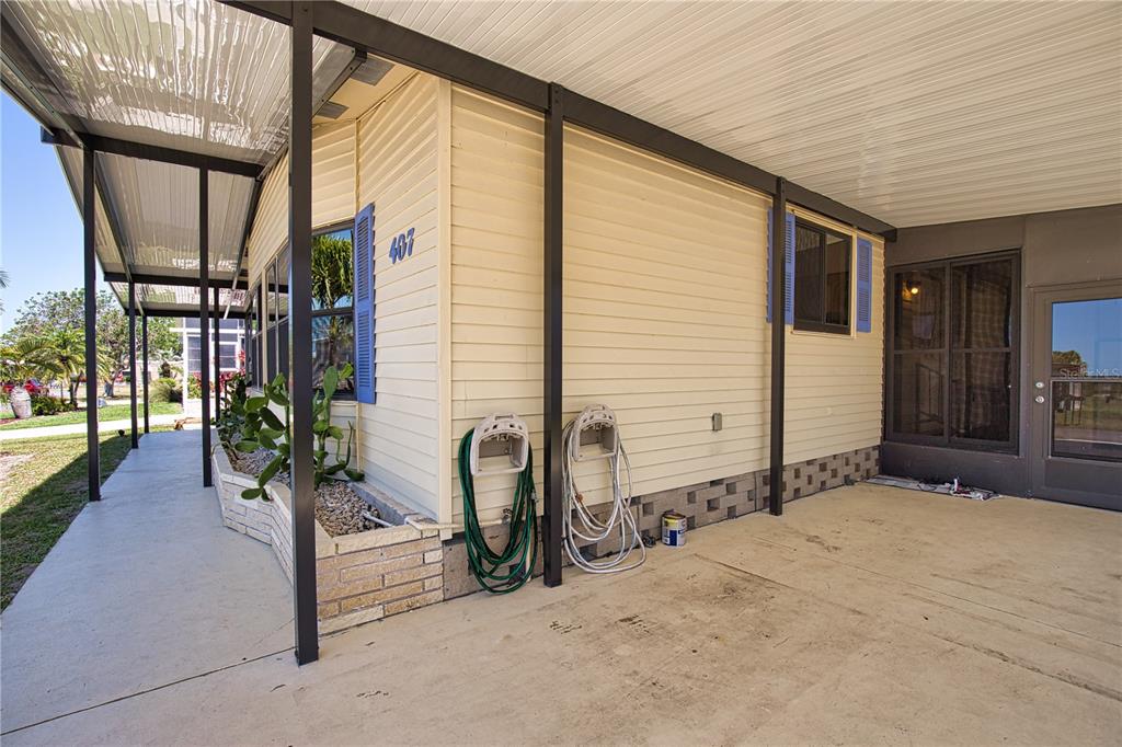 A covered carport area features beige siding, a concrete floor, and a brick planter box — 407 MADONNA, NORTH PORT, FL