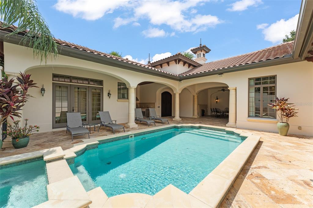A swimming pool and spa sit on a stone patio outside a Mediterranean-style home — 4819 ALEXANDRA GARDEN COURT, WINDERMERE, FL