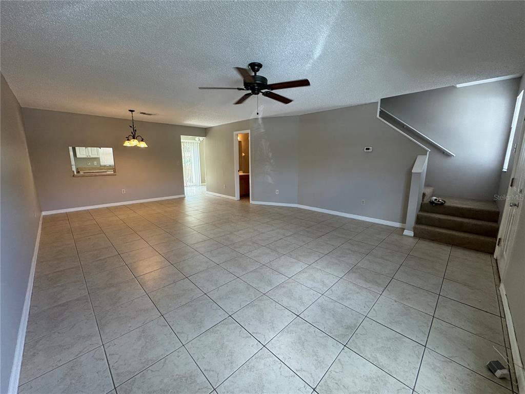 An open-concept living area features light-colored tile flooring, gray walls, and a carpeted staircase — 1643 SANDY POINT SQUARE UNIT 72, ORLANDO, FL