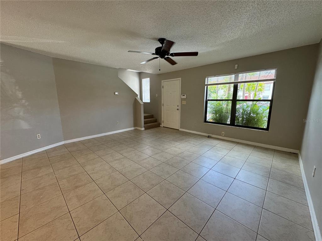 An empty living room features beige tile flooring, a ceiling fan, and a staircase — 1643 SANDY POINT SQUARE UNIT 72, ORLANDO, FL