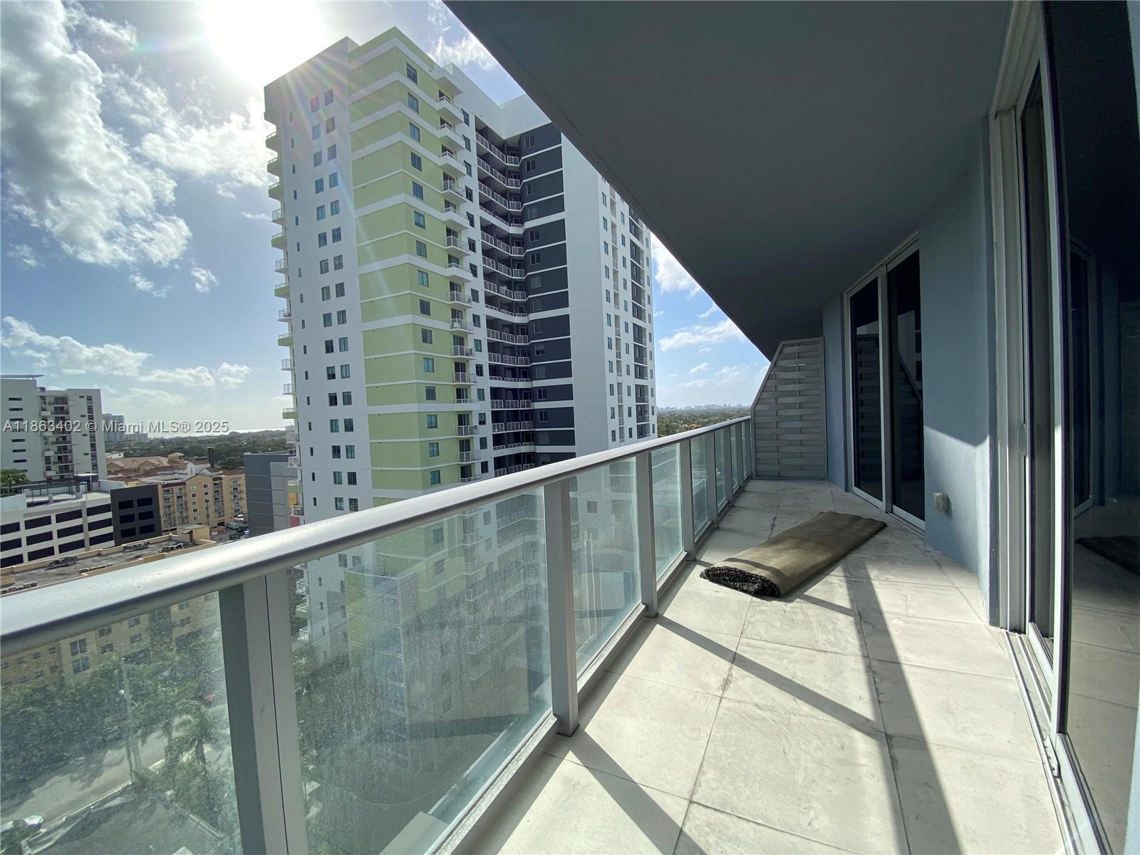 A high-rise balcony features a glass railing, tiled flooring, and views of neighboring apartment buildings — 1010 SW 2 AVE # 1110, Miami FL 33130, MIAMI, FL
