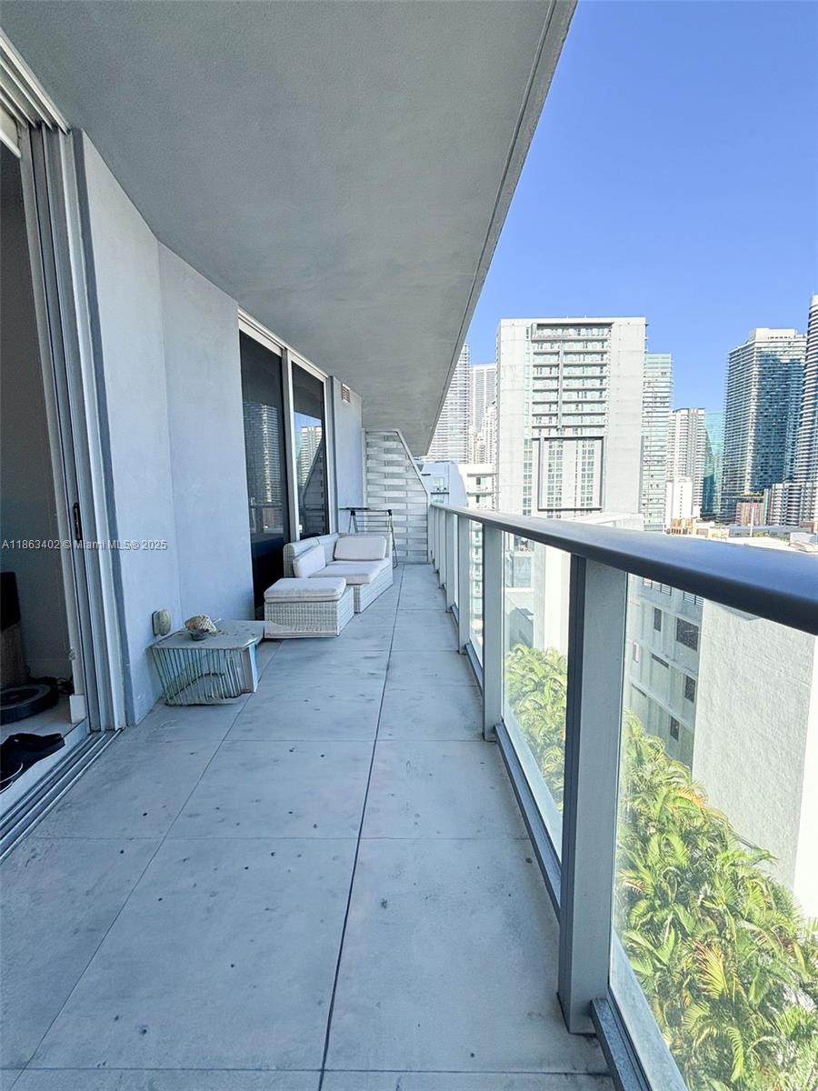 A balcony features concrete flooring, a glass railing, and outdoor furniture overlooking a city skyline — 1010 SW 2 AVE # 1110, Miami FL 33130, MIAMI, FL