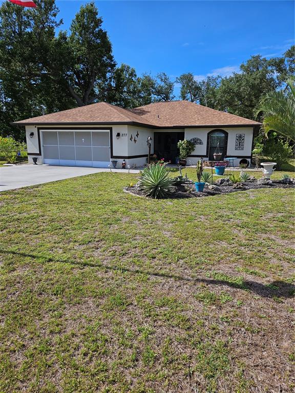 A single-story house with a two-car garage, tan stucco walls, and a brown shingled roof — 277 ALBATROSS ROAD, ROTONDA WEST, FL