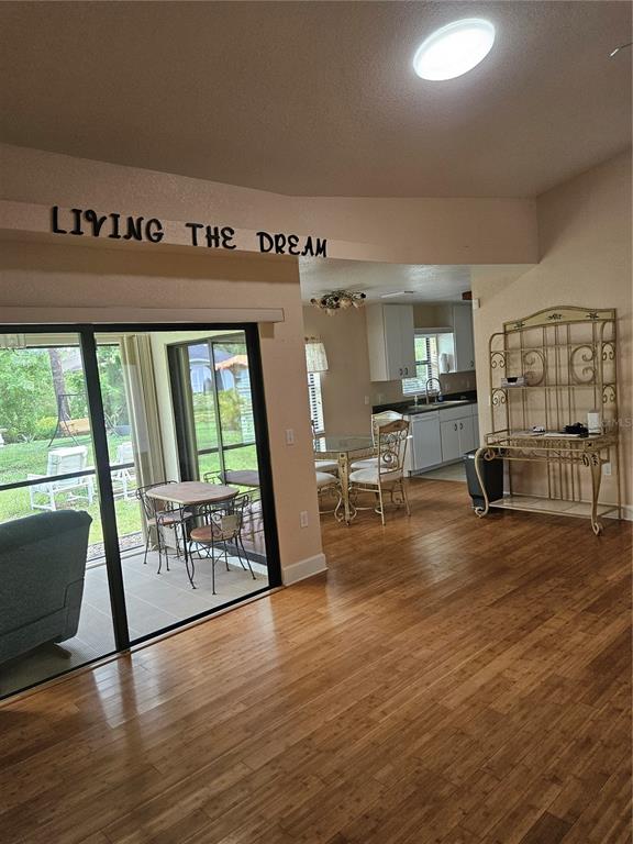 A living area with wood flooring leads to a kitchen and a screened-in patio — 277 ALBATROSS ROAD, ROTONDA WEST, FL