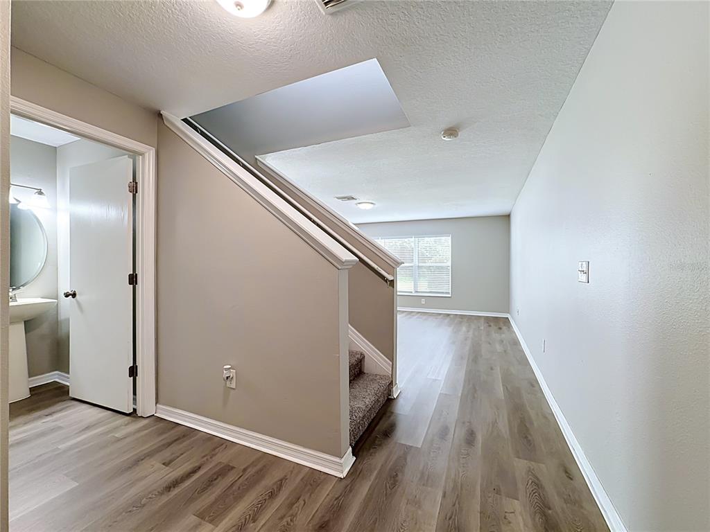 A view of a hallway with wood-look flooring, a staircase, and an adjacent bathroom door — 6320 MAGNOLIA TRAILS LANE, GIBSONTON, FL